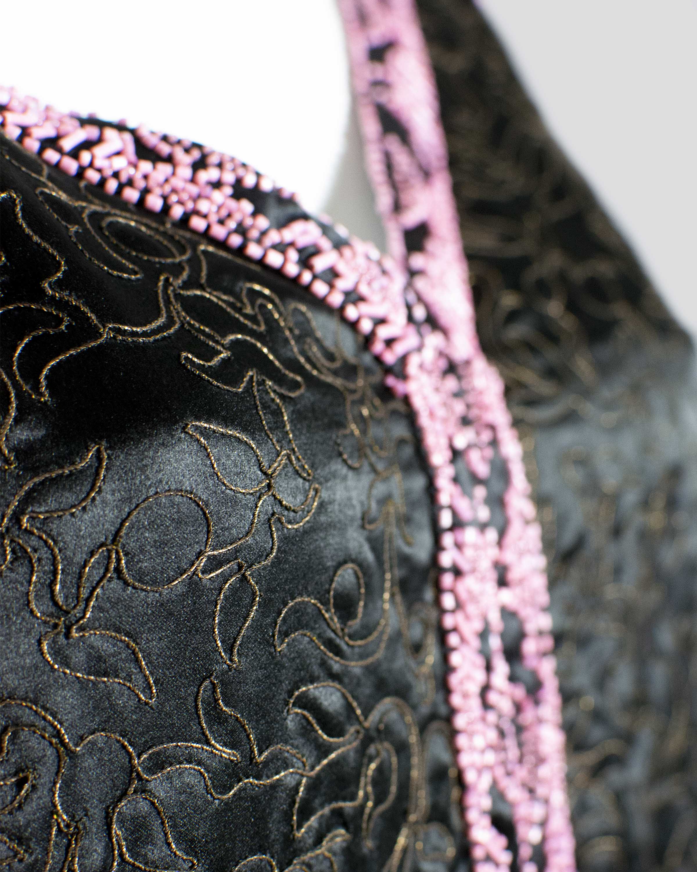 Detail photograph of the gold cording detail and pink beading around the neckline of a black satin sleeveless dress