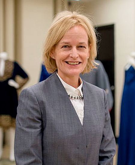 Dr. Ingrid E. Mida smiling at the camera wearing a grey blazer and white collared shirt