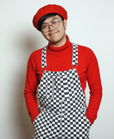Steve posing wearing a red beret, a red turtleneck and black and white checkered overalls
