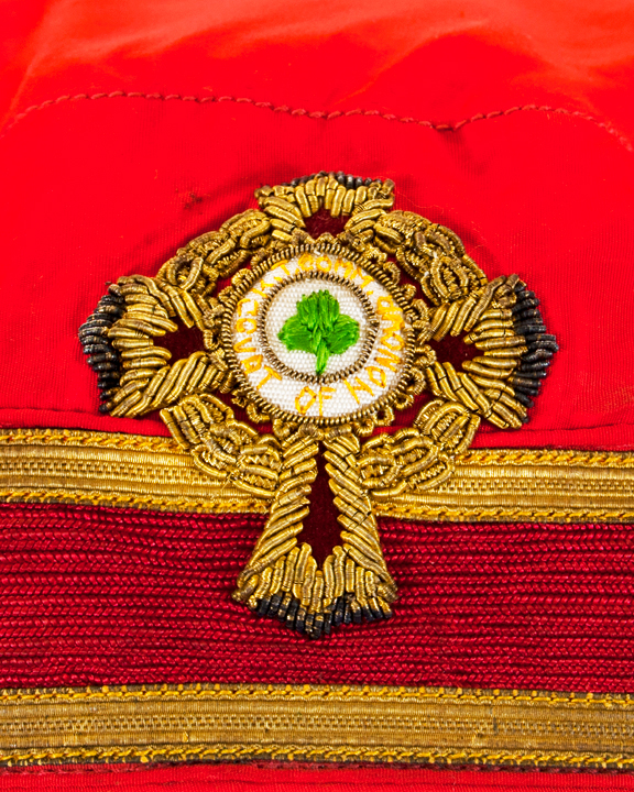 Gold thread emblem on the front of a cherry red men's ceremonial cap