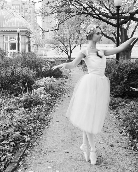Young woman wearing a white body suit and long white tutu in front of Allan Gardens Conservatory