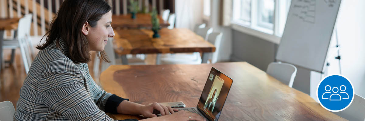 An employee sitting at a table on her laptop in a virtual meeting.
