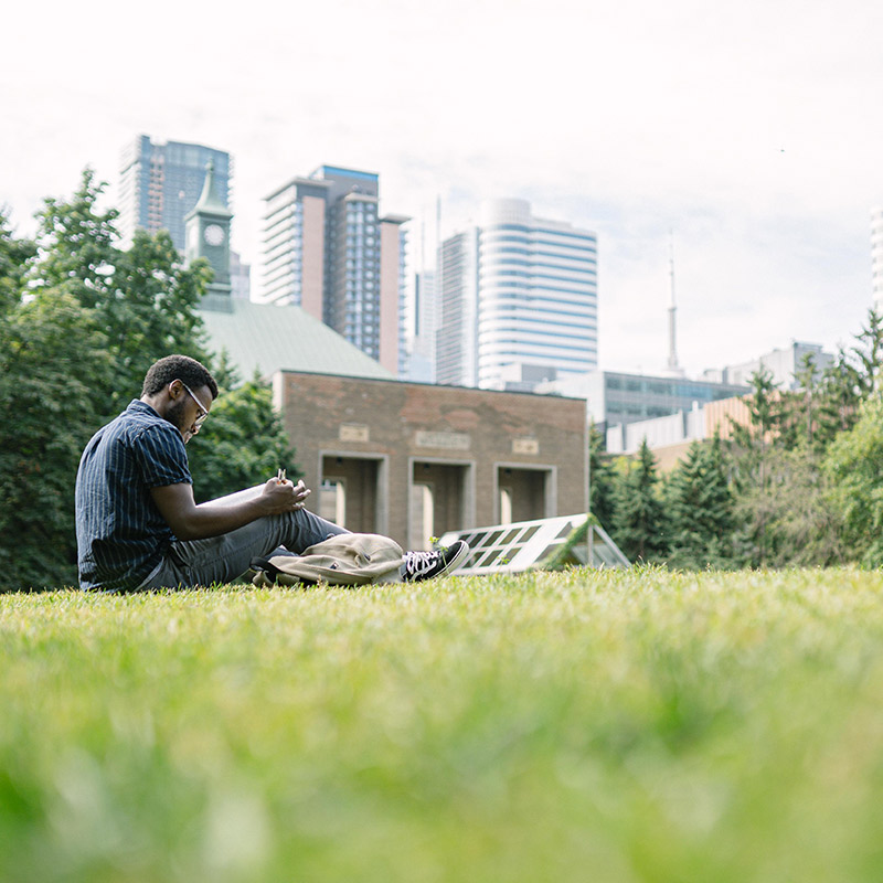 Toronto Metropolitan University student reading on the grass in the Quad on a sunny day.