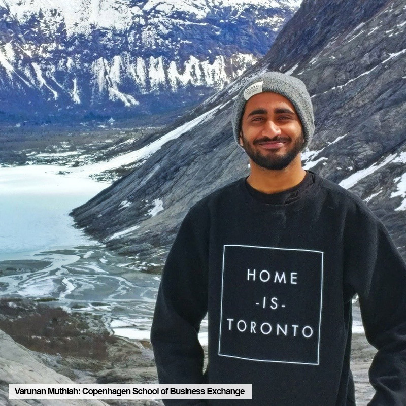 Toronto Metropolitan University TRSM student, Varunan Muthiah, wearing "Toronto is Home" sweater, poses with mountain range during a trip to Norway while on exchange at Copenhagen School of Business.