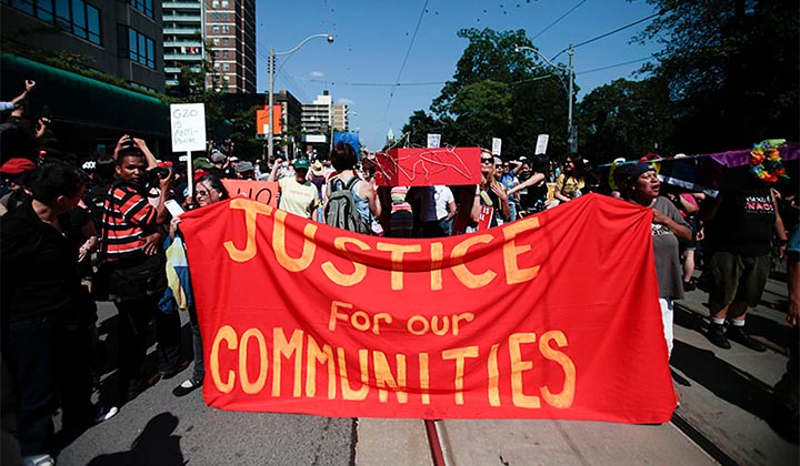People march on a Toronto street, holding a "Justice for our Communities" banner
