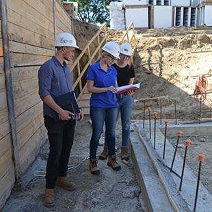 Three graduate students wearing hard hats on construction site