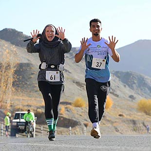 Kate McKenzie and male marathon contestant running on road in Afghanistan