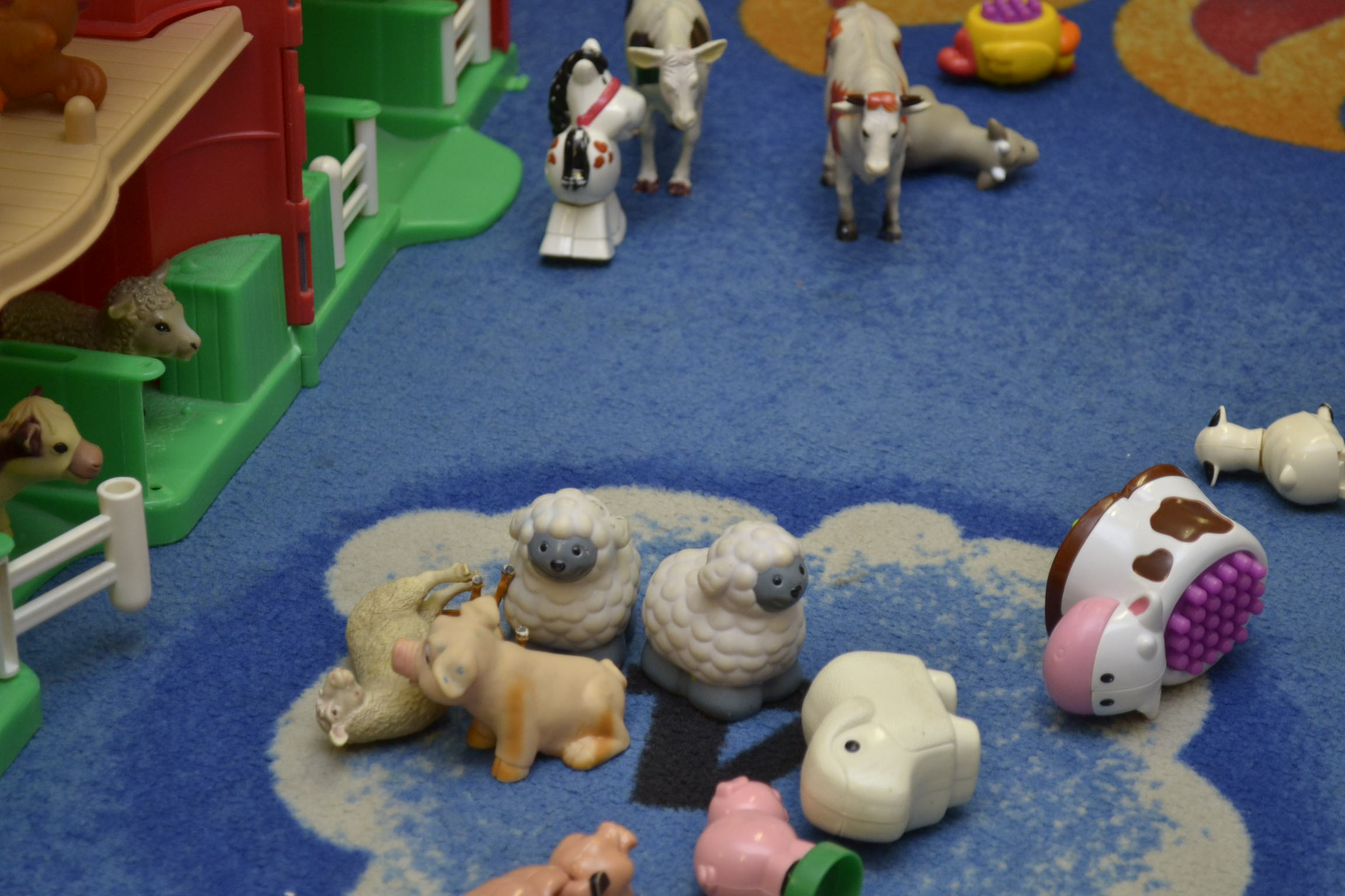 Divers animaux de la ferme en plastique pour enfants sont éparpillés sur un tapis dans un centre de garde d’enfants.