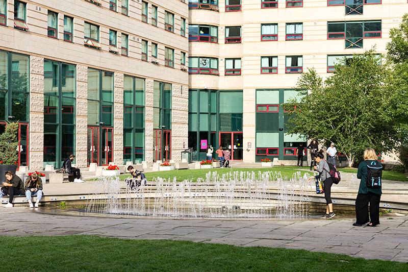 The front of Pitman Hall, with a fountain in the foreground and students walking around the property