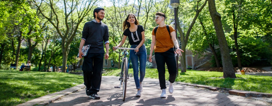 Three students walking on campus, one is pushing her bicycle.