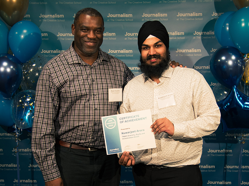 Kuwarjeet Arora holds a certificate while standing with Rod Charles in front of a blue backdrop that repeats, "Journalism at The Creative School."
