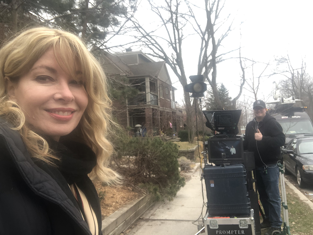 Cynthia Mulligan does a standup on the sidewalk outside of her home. Her cameraman drives the van over for the physically-distant arrangement (Cynthia Mulligan).