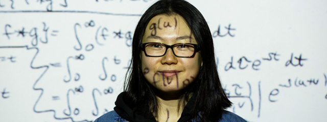 Mth graduate student standing in front of projector with math equations projected on her face.