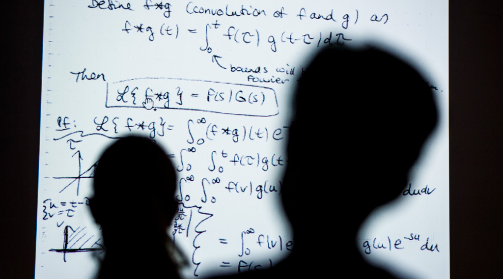 Undergraduate student's heads casting shadows on equations projected onto class board.