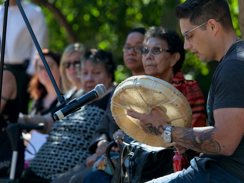 Social work student Joshua Fisher drumming and singing an honour song at the plaque unveiling