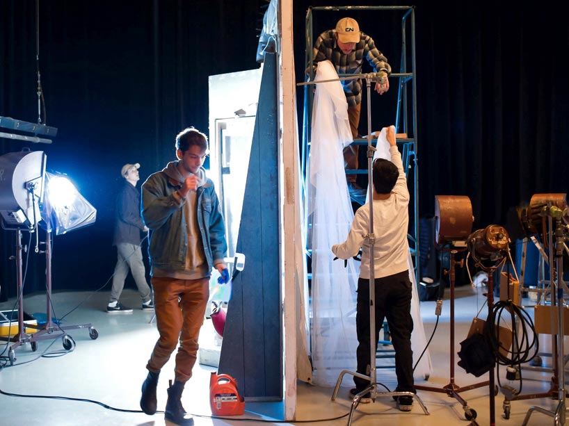 One student, left, walks by two other students who are adjusting drapery on a film set