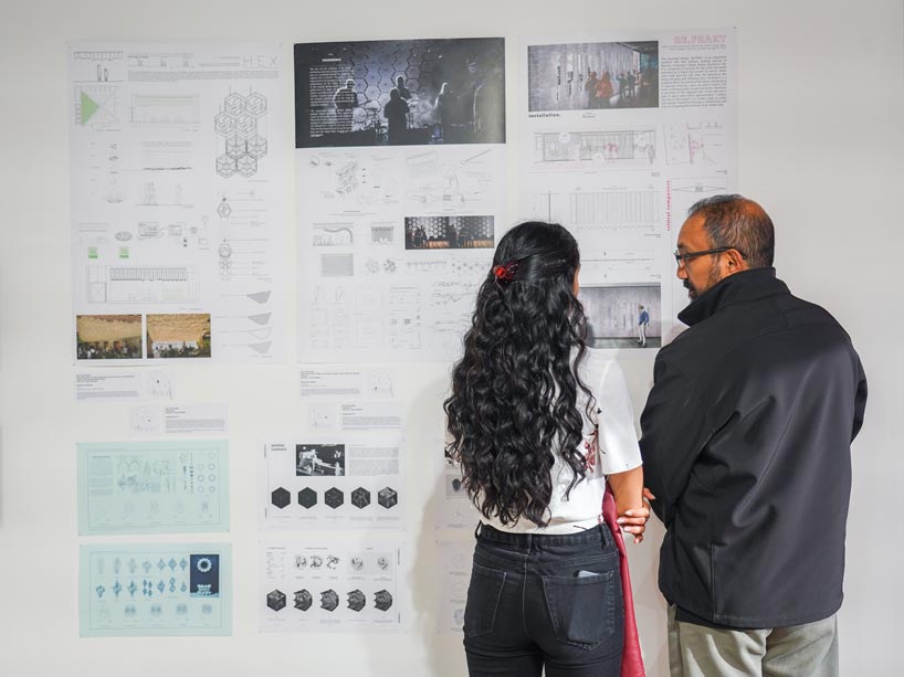 A man and a woman with their back to the camera looking at a wall of architectural drawings