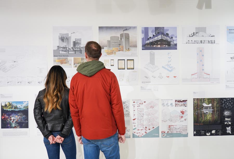 A man and a woman with their backs to the camera looking at a wall of architectural drawings