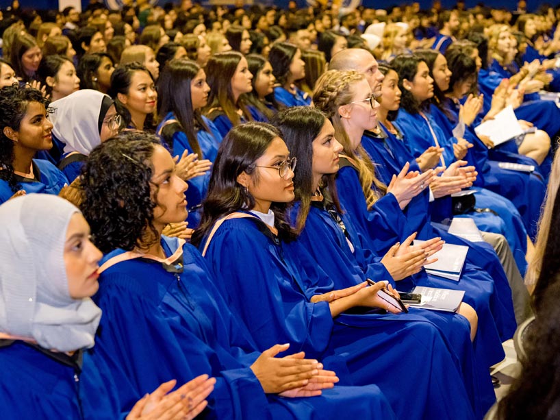 Students dressed in convocation gowns, clapping during the ceremony