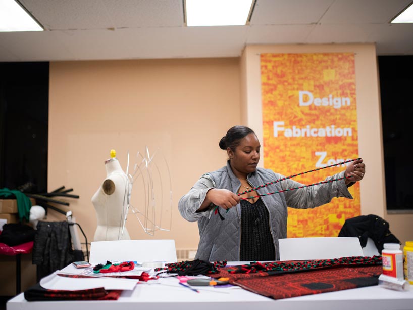 Candice Dixon works with fabric on a wide table with mannequin in the background