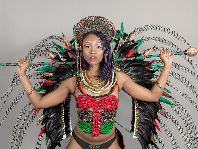 A woman wearing a colourful Carnival costume holding a cane behind her shoulders