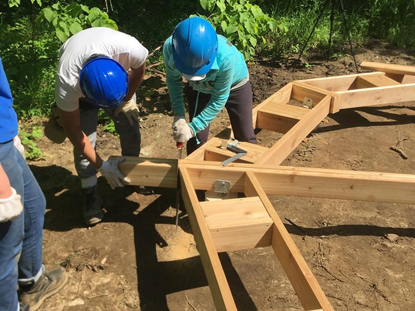 Two students wearing hard hats drilling into wooden beams