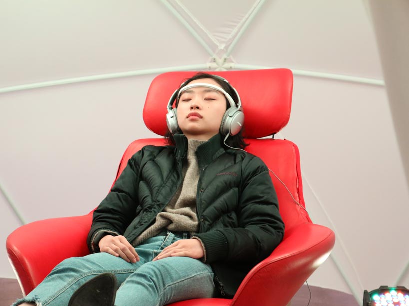 A person sits with their eyes closed and headphones on, listening to the LUCID technology in a red chair
