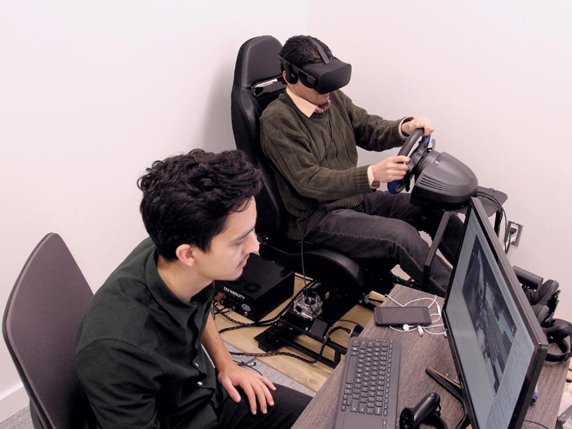 One student wears a VR headset and the other works on a computer
