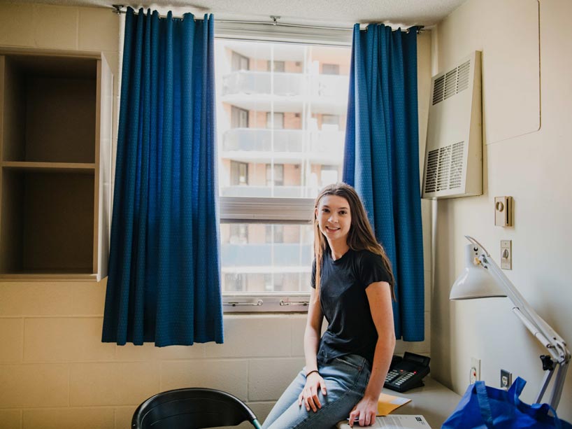 A student leans on desk in front of window in residence room