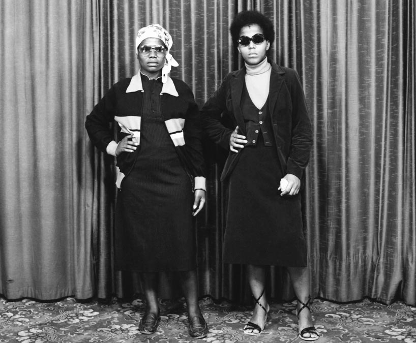 Black and white photo of two Black women standing with their right hands on their hips