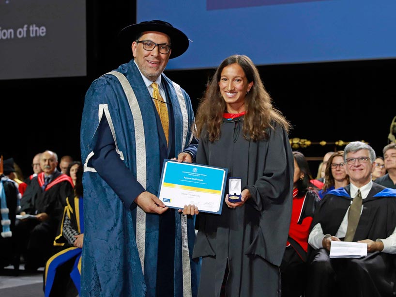 From left: President Mohamed Lachemi and Meera Govindasamy holding her degree and gold medal on stage at convocation
