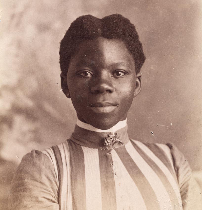A sepia-toned image of a Black South African woman wearing a high collared, striped dress