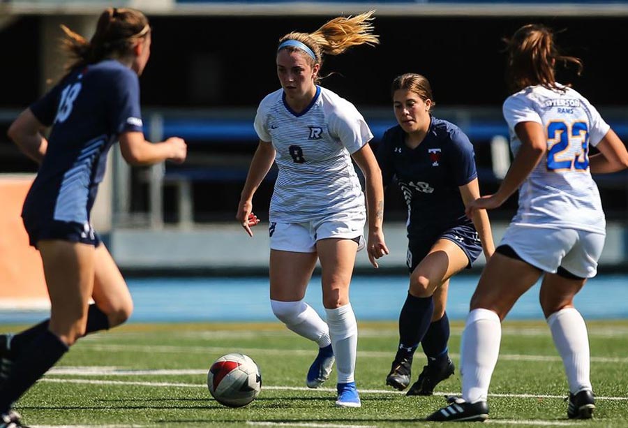 A Ryerson Rams female soccer player looks to pass to her teammate while being run in on by two opposing players