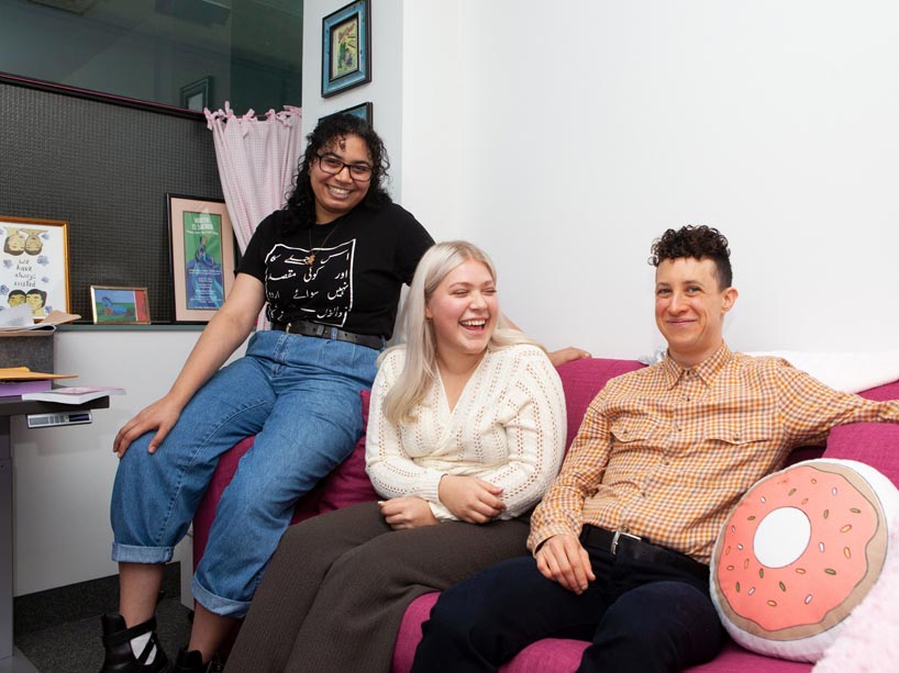 Students Saadia Khan and Cat Carpenter sit on a bright pink couch next to trans studies course professor Marty Fink, far right