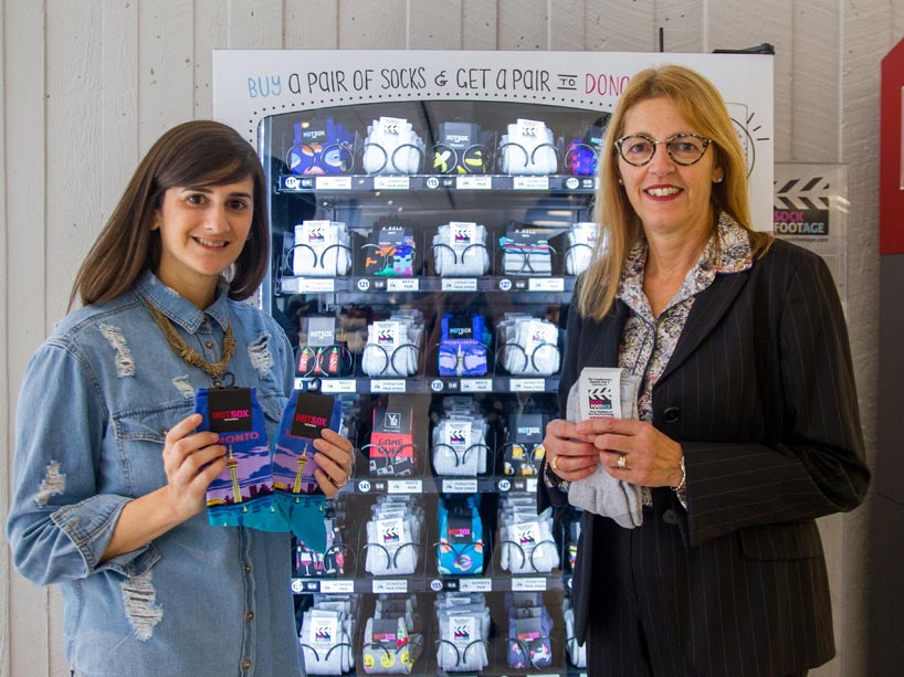 From left: Marisa Sheff and Voula Cocolakis holding a pair of socks in front of a sock vending machine