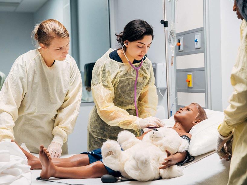 Three nursing students work with a child-sized mannequin in a hospital room