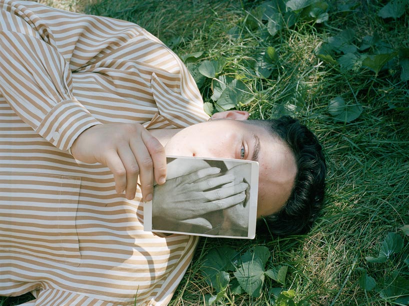 A person lying on the grass holding a black and white photograph of a hand in front of their face