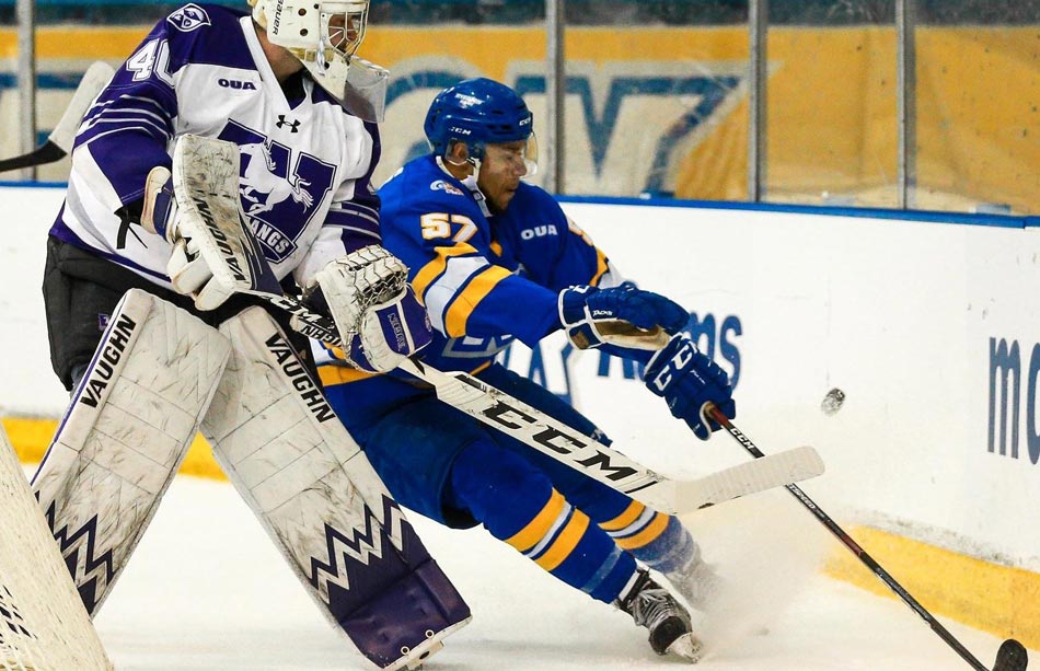 A male hockey goalie blocks an opposing hockey player trying to get the puck against the boards