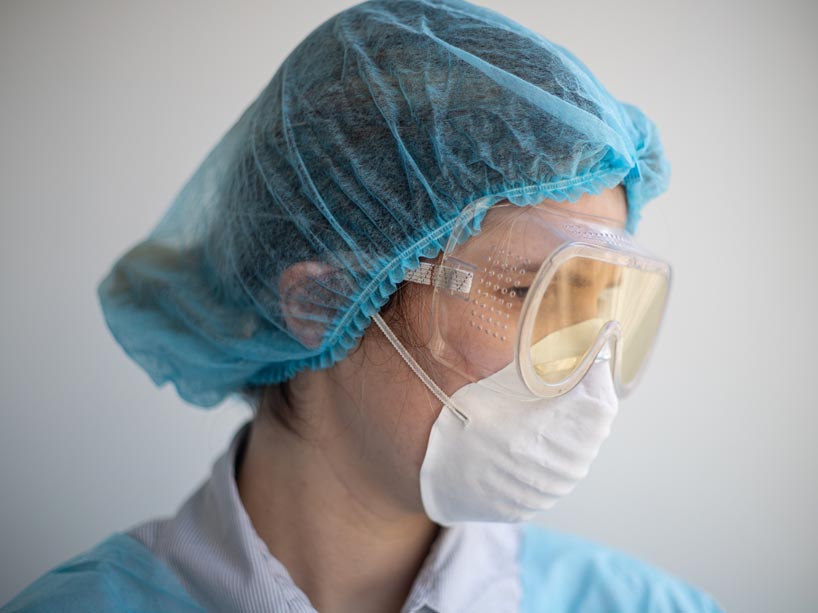 A nurse wearing protective goggles, face mask and hair covering