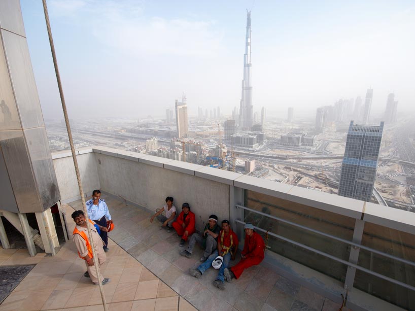 Indian construction workers rest atop tall building, the Dubai skyline in the distance