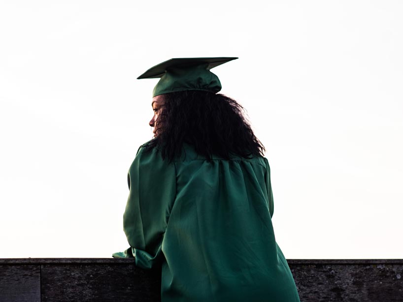 A graduate wearing a robe and cap with her back to the camera, looking off