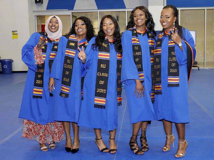 Five Black woman graduates wearing blue convocation gowns and Kente stoles