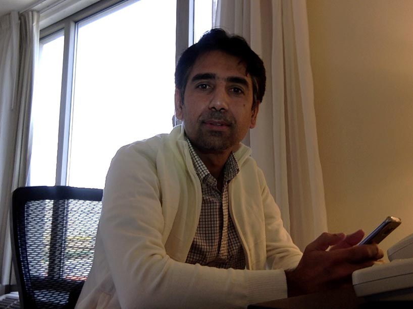 Mubariz Tariq sits at a desk holding his cell phone.
