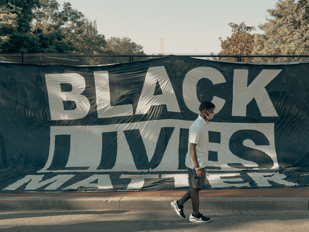 A man in a face mask walks by a Black Lives Matter banner