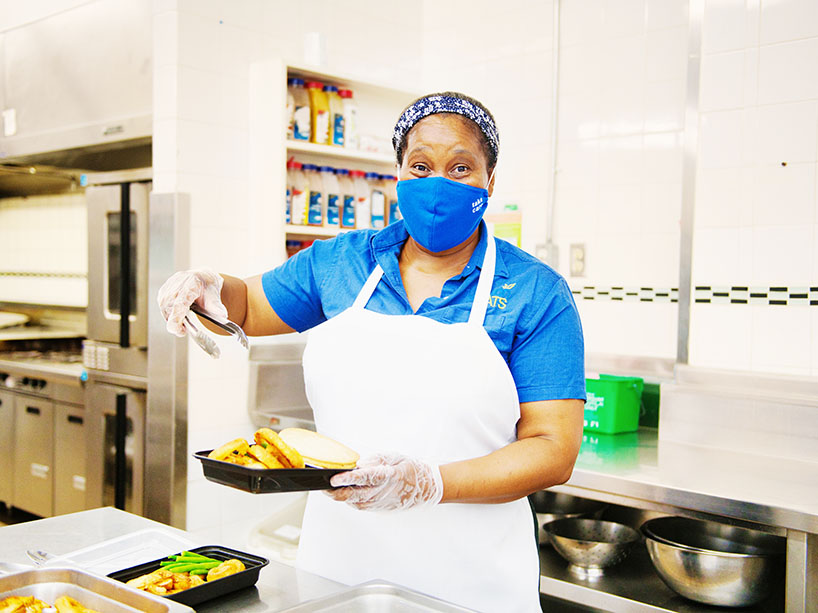 A woman wearing a mask, gloves and apron putting food in a takeaway container