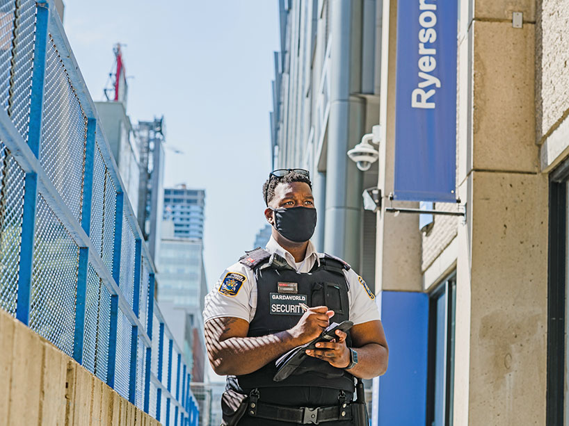A security guard wearing a mask and taking notes on campus