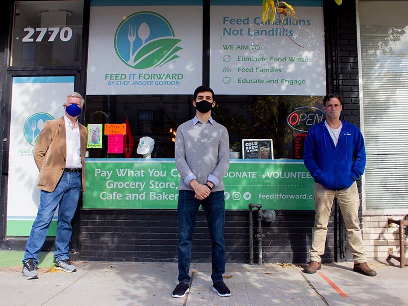 Three men, wearing masks, stand in front of a pay-what-you-can grocery store