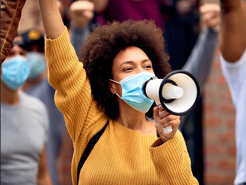 A young woman at a protest speaks into a loudspeaker with a mask on