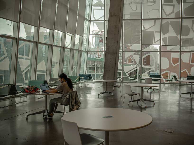 A student wearing a mask sits at a table in the Student Learning Centre working on a laptop.