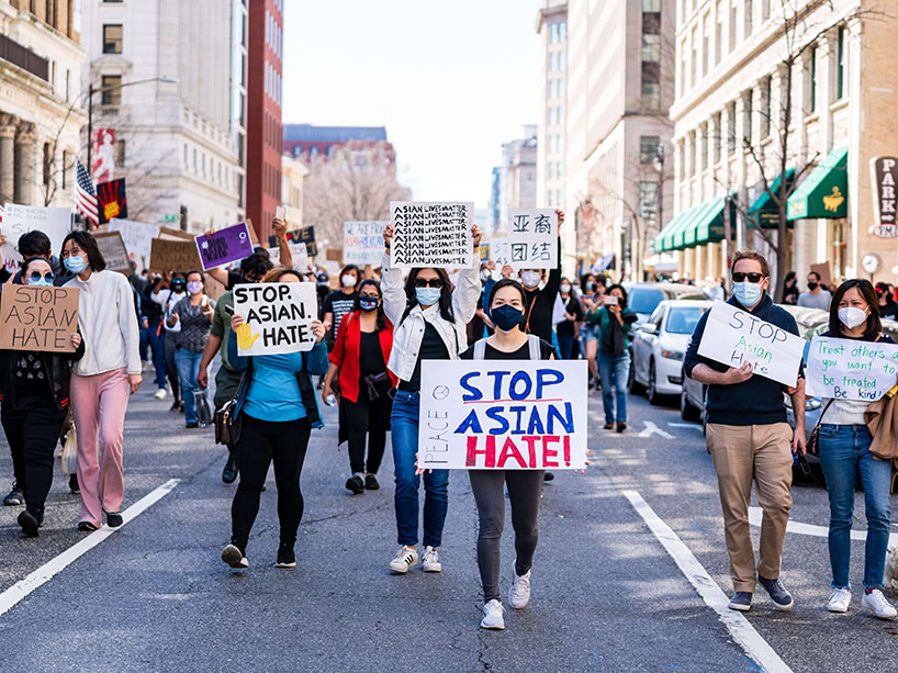 A group with masks on marches in protest with signs that say “stop Asian hate.”